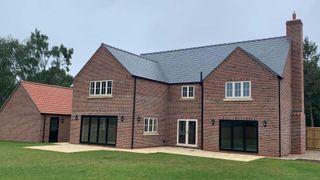 A large brick-clad detached home with two prominent gable ends. The roof is clad in slate, sourced by Northern Slate.