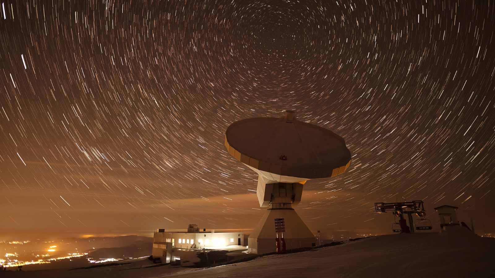 A satellite dish points up at the night sky in a long exposure image