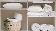 A linen closet with pillows, rolled towels, and bed linen on display.