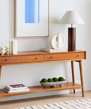 An entryway with a wooden storage console, with a cream and dark wooden lamp on top of it and a blue and white wall art print above it