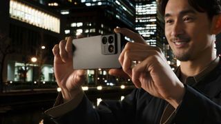 Sony Xperia 1 VIII held up by a person taking a photo in front of a nighttime cityscape