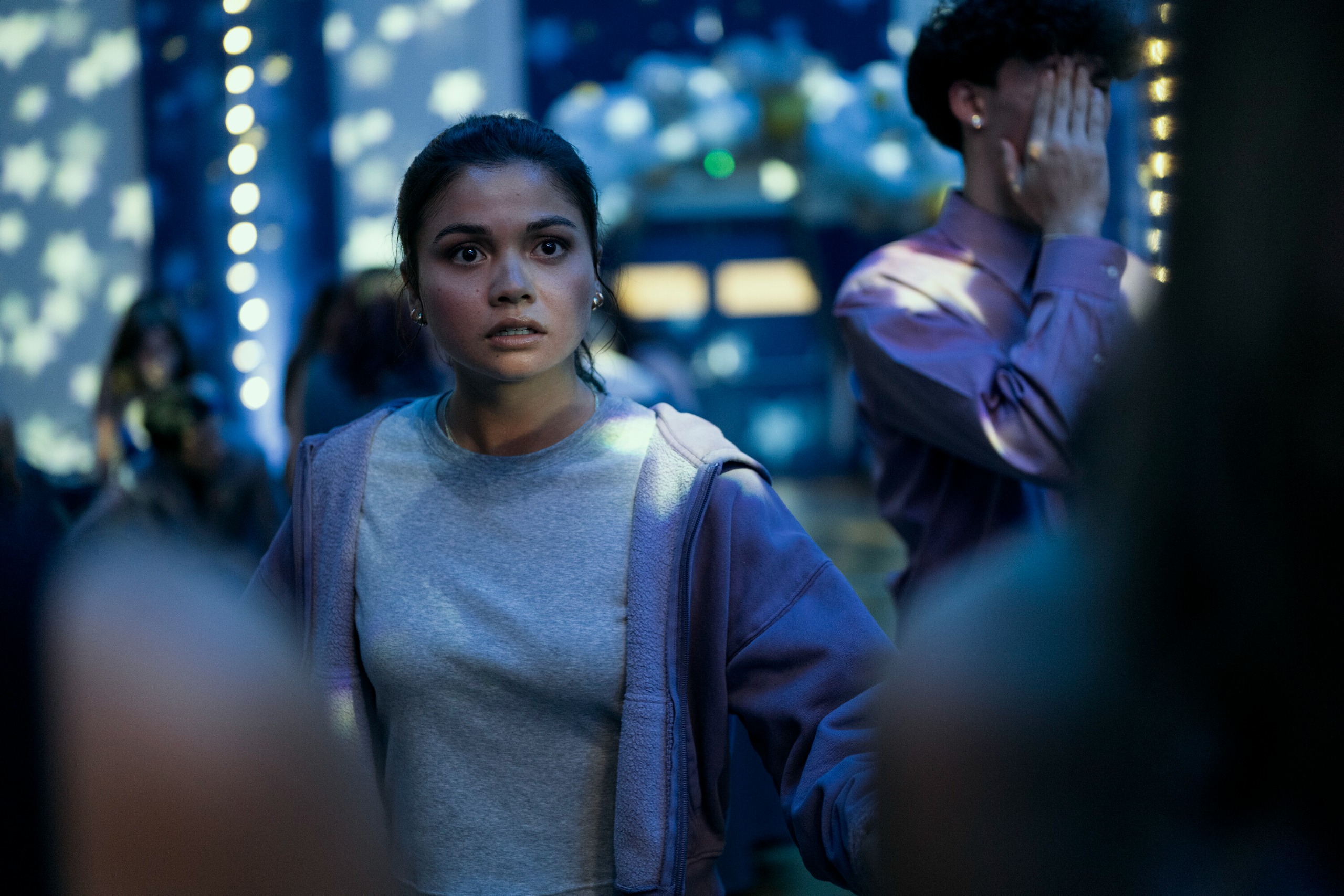 A teenage girl in a hoodie and T-shirt (Siena Agudong as Sue Snell) stands in the middle of a high school prom, in Prime Video's 'Carrie'.