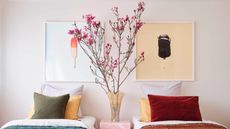 bedroom with twin beds in colorful bedding, two artworks above bed, and a vase on the bedside table filled with large blossom branches