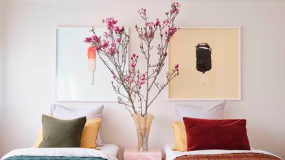 bedroom with twin beds in colorful bedding, two artworks above bed, and a vase on the bedside table filled with large blossom branches