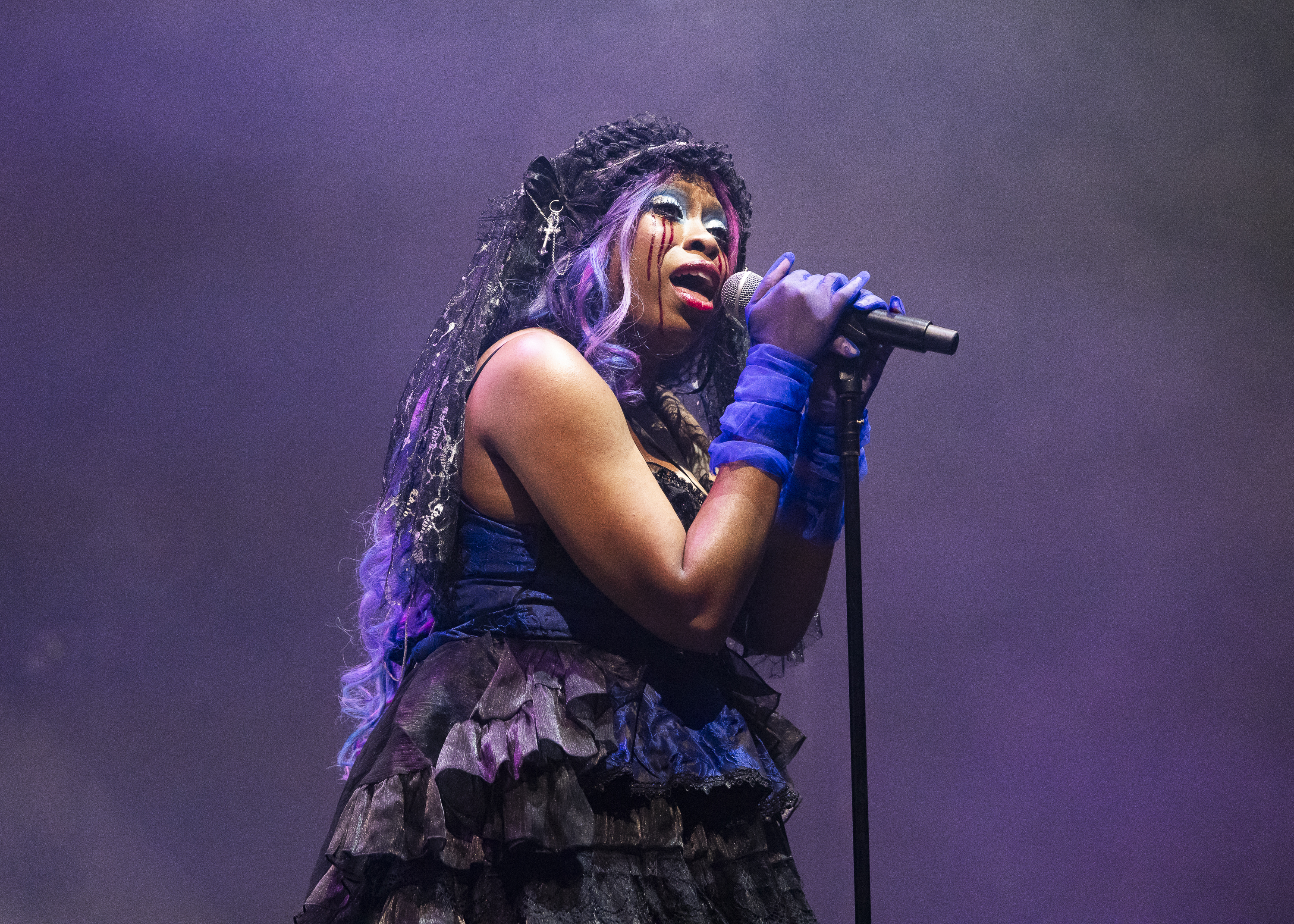 hemlocke springs performs on stage in a purple and black 80s like dress