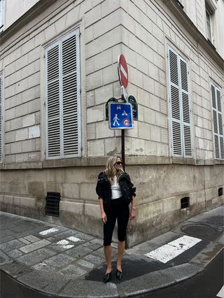 Eliza Huber trägt in Paris eine schwarze, sportliche Jacke von Proenza Schouler mit einem weißen Tanktop, einer schwarzen Caprihose und schwarzen Prada-Heels.