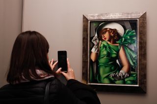 A woman takes a photo on her smartphone of a painting by Tamara de Lempicka