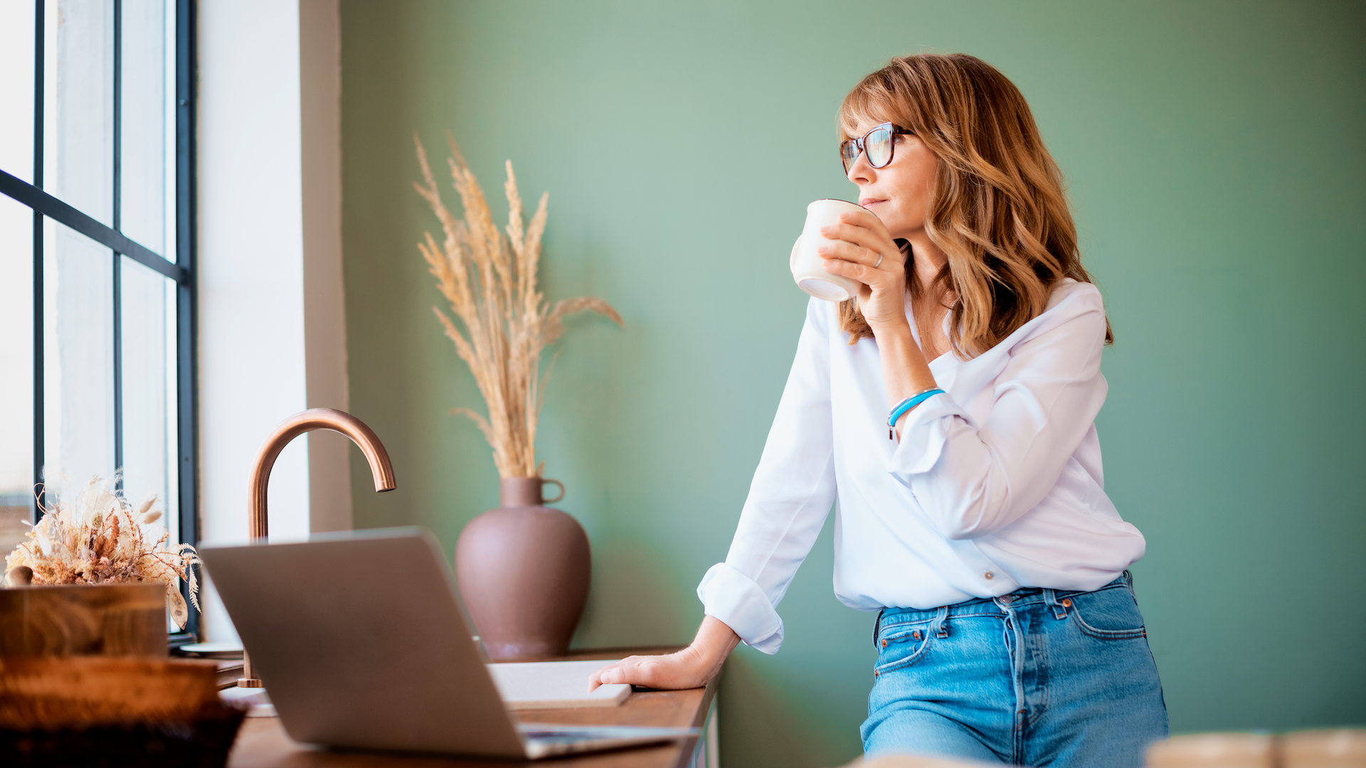 Woman looking out window while using laptop