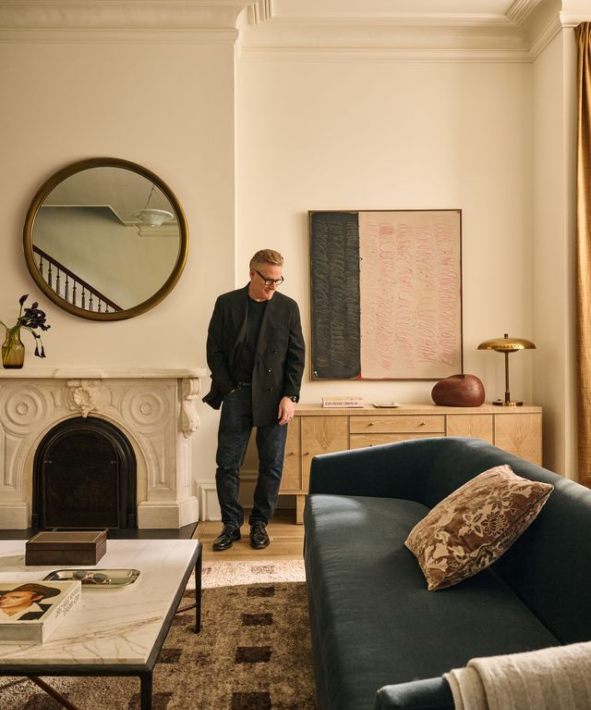 a man standing in a living room with a blue couch, a marble coffee table, a decorative fireplace, and a mirror hanging from the wall
