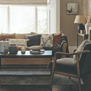 A beige-painted living room with a light brown sofa and variously coloured and patterned scatter cushions