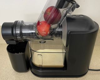 Philips Viva Masticating Juicer with two whole red apples in chute and freshly-pressed juice