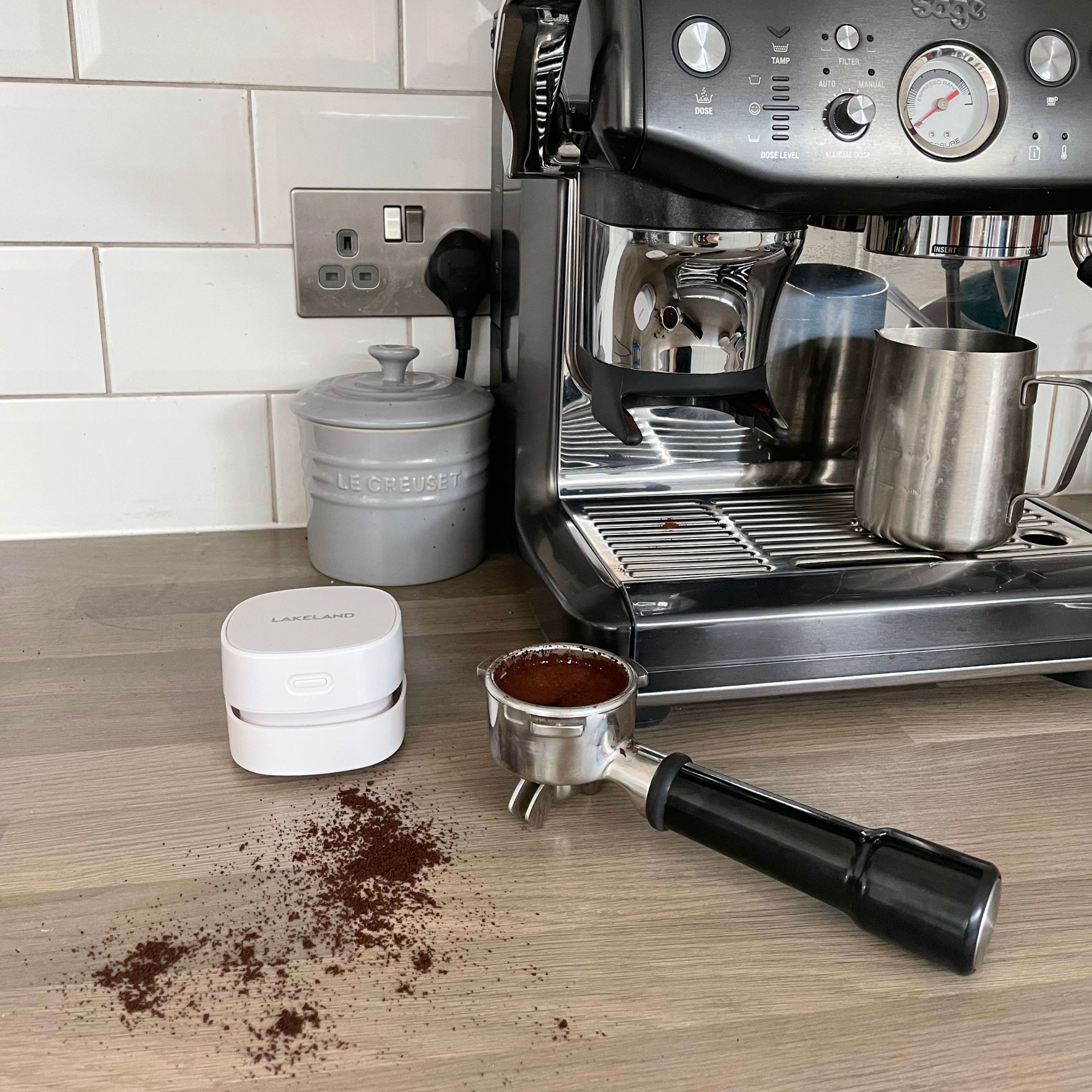 Lakeland mini countertop vacuum on a kitchen counter by a sage coffee machine, with coffee grounds on the side
