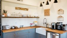 An image for how to organize a small kitchen with too much stuff showing a wooden and blue corner kitchen with open wooden shelf storage and tray orgaziners on counters