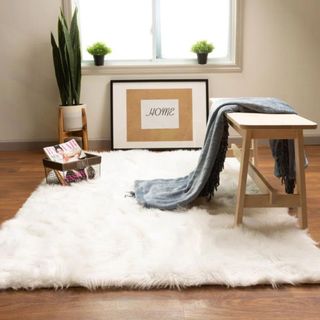 A white faux fur rug sits on a wooden floor, next to a table and photo frames