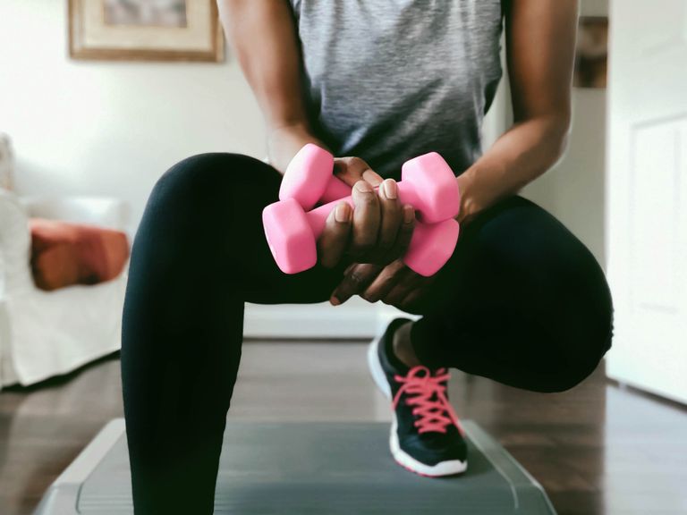 black woman working out at home with dumbbells and aerobic step