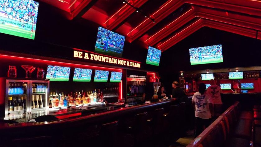 The inside of BLOODSports, a sports and horror dive bar, with more than 10 TVs in a dimly lit, red hued environment. 