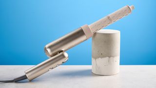 The Dreame Pocket Neo in gold with curling attachment photographed in front of a blue background.