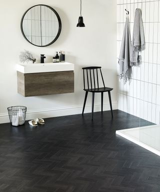 Black parquet-look vinyl flooring in a shower room with white walls and a wooden sink stand next to a black chair