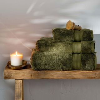 dark green bath towels with candle on wooden bench