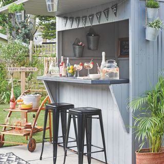 outdoor bar/cooking area painted in pale grey, black metal stools, small bar on wheels, bunting
