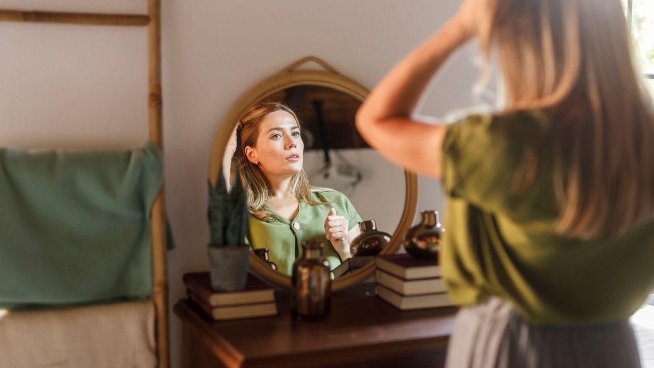 Woman looking in make up mirror, adjusting hair and make up at home, representing how to get rid of a cold sore