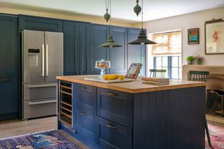 kitchen with blue island and cabinets and American fridge freezer with oriental rugs on floor and stone fireplace behind