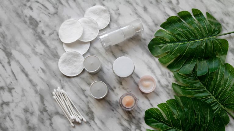 Pots of skincare with cotton buds on a marble backdrop
