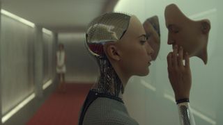 A still from the movie Ex Machina in which the character Ava touches synthetic faces attached to a wall.