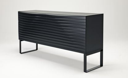 A black horizontal rectangular drawer featuring a ripple effect front and 2 open square legs photographed from the right angle agasint a white background