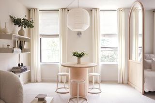 room in light neutral tones with round table and chairs in the middle, in front of windows