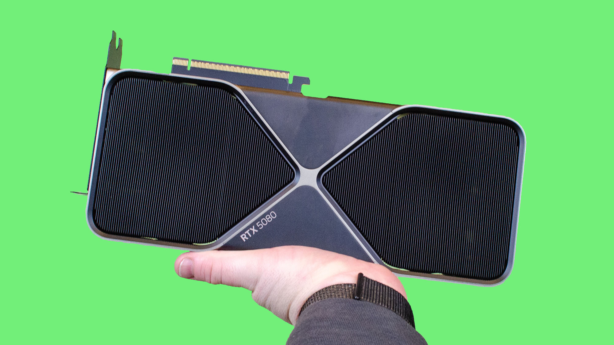 A masculine hand holding up an Nvidia GeForce RTX 5080 against a green background