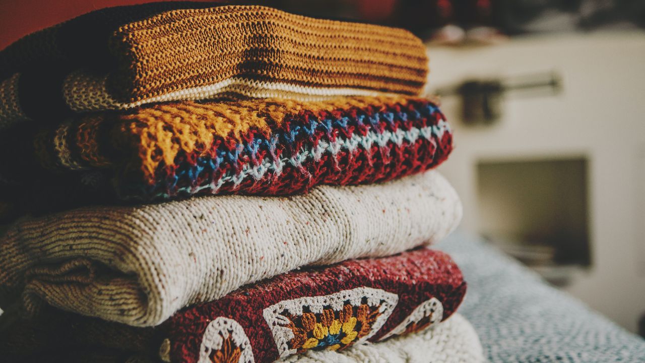 a pile of women&#039;s winter sweaters on a bed