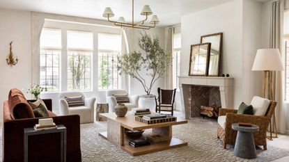traditional neutral farmhouse living room by marie flanigan with a fireplace, large rustic sofa, wooden coffee table, olive tree, and two white arm chairs