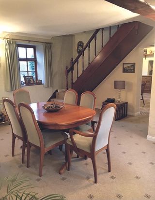 Before shot of dining room with dark wood table and chairs, patterned beige carpet and dark wood staircase