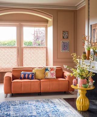 A small living room with peach walls and a peach couch with colorful cushions