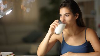 Woman sat at a table drinking a glass of milk before going to bed