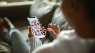 An image of a person lying on a couch, buying clothing on a phone shopping app