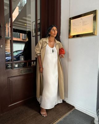 @monikh wearing a white shift dress and trench coat