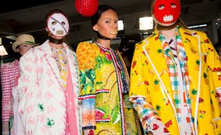 Models wear crab printed pink and white coat, yellow and orange beaded dress, and fruit printed vinyl yellow coat with checked jacket