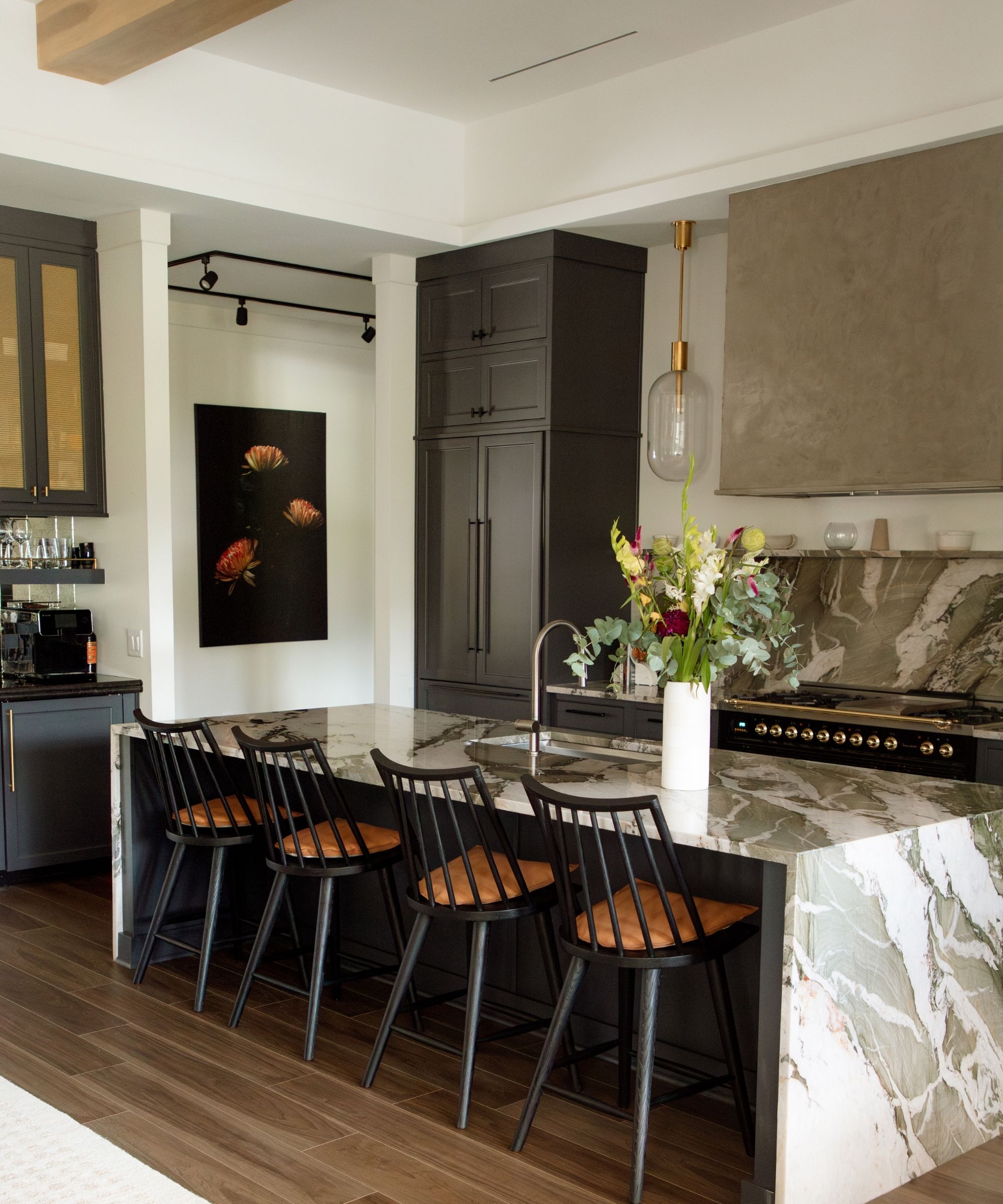 A kitchen with blue cabinets, a marble island, and layered lighting
