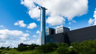 a tall silver rocket in front of a long low building and blue sky