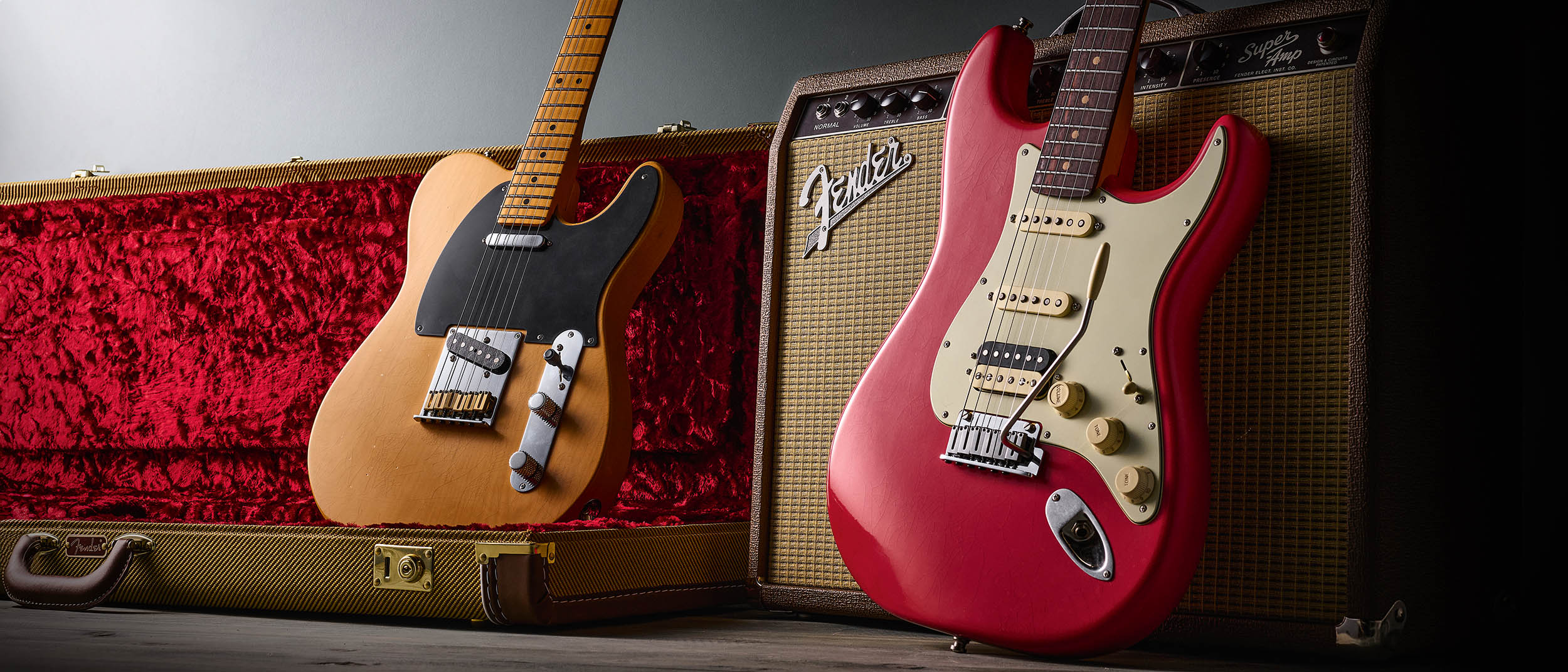Fender American Ultra Luxe Vintage '50s Telecaster and Vintage '60s Stratocaster HSS photographed against a Fender combo and their tweed-covered case.