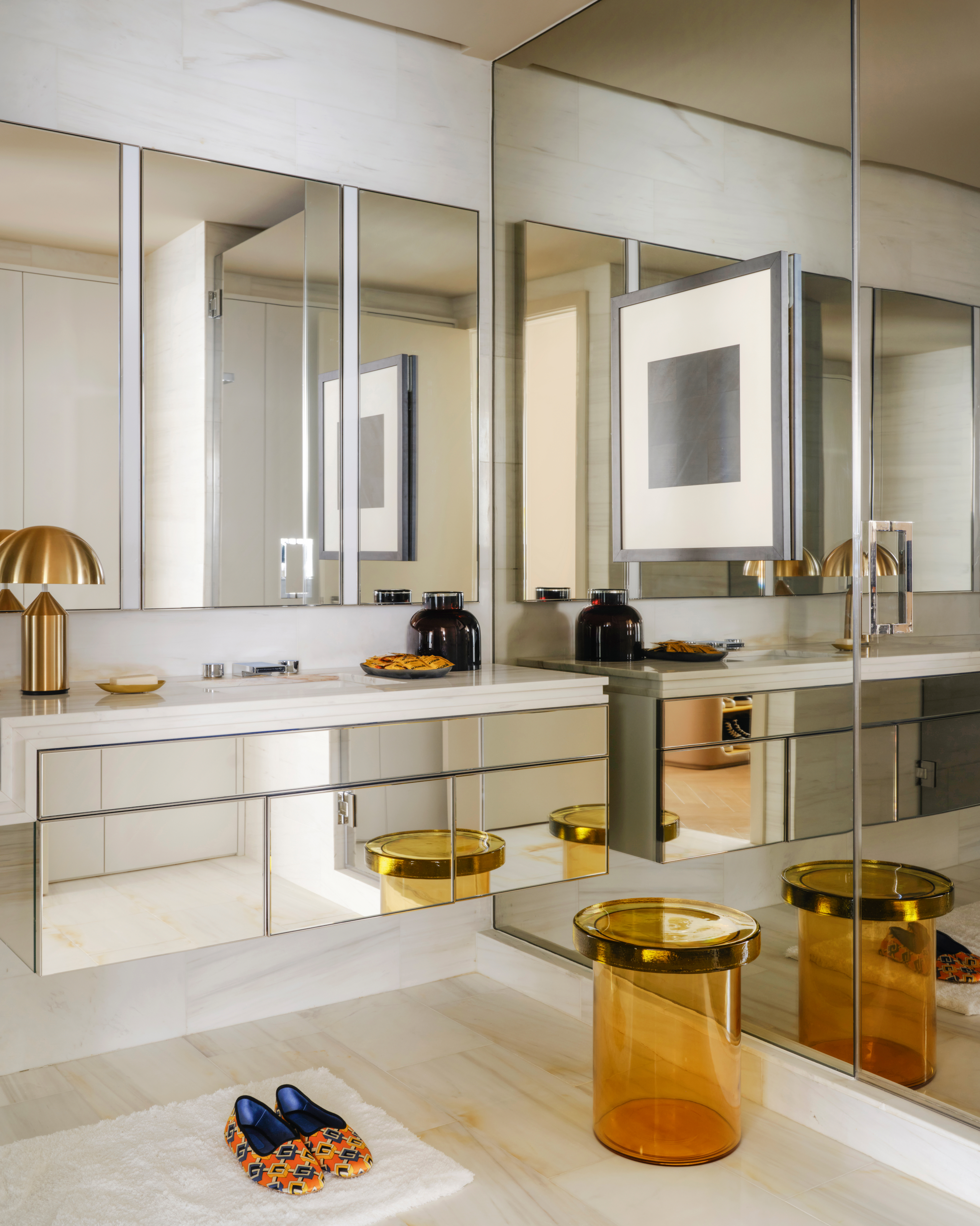 Bathroom with mirrored walls and vanity, amber glass stool and brass table lamp