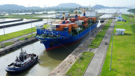 A cargo ship and tugboat pass through the Cocoli Locks of the Panama Canal.