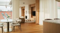 Image of an open plan home with a kitchen, dining area, and living room all in view. There are wooden floors, wooden walls, large white curtains, and lots of curved details. 