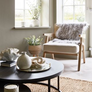 A neutral-coloured living room with an accent chair and a black round coffee table displaying a curated selection of decor