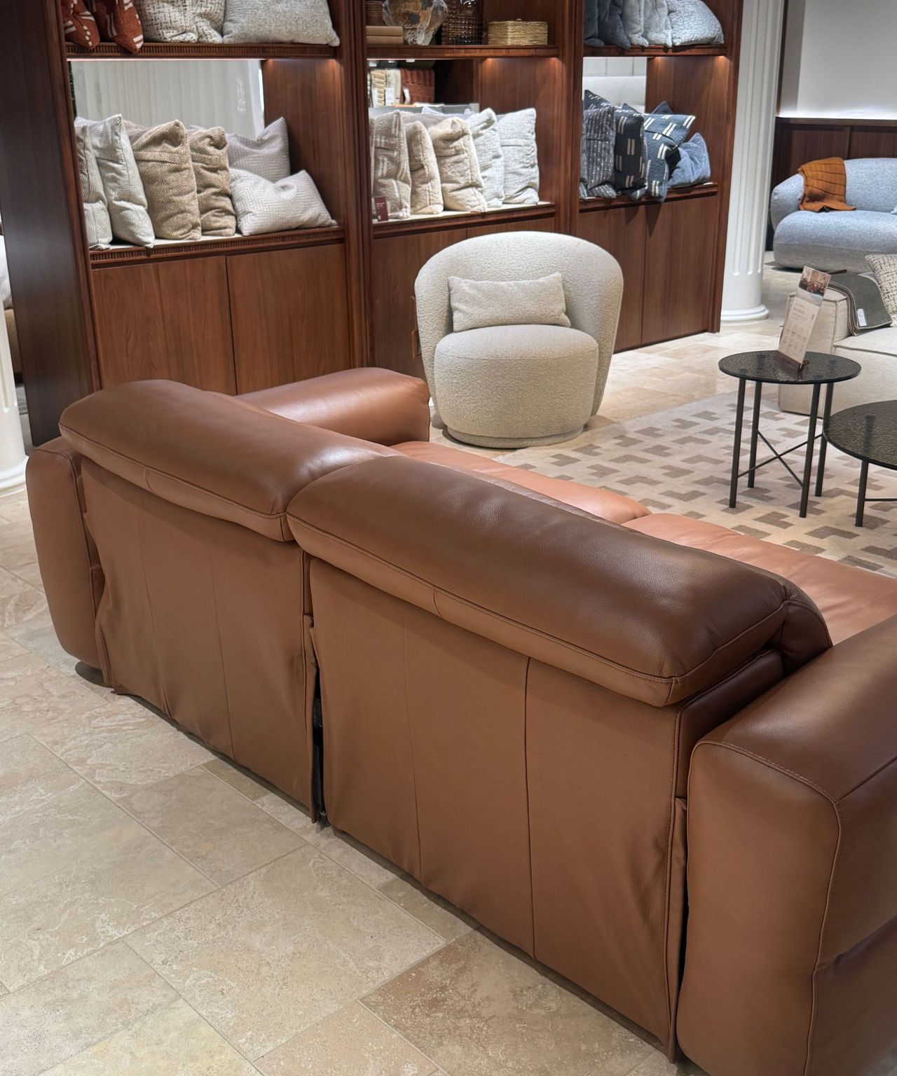the back of tan leather sofa in front of timber cabinets filled with cushions