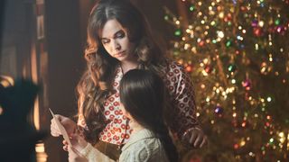 Megan Cusack in a floral top as Nancy with Francesca Fullilove as Colette stand in front of a Christmas tree in Call the Midwife.
