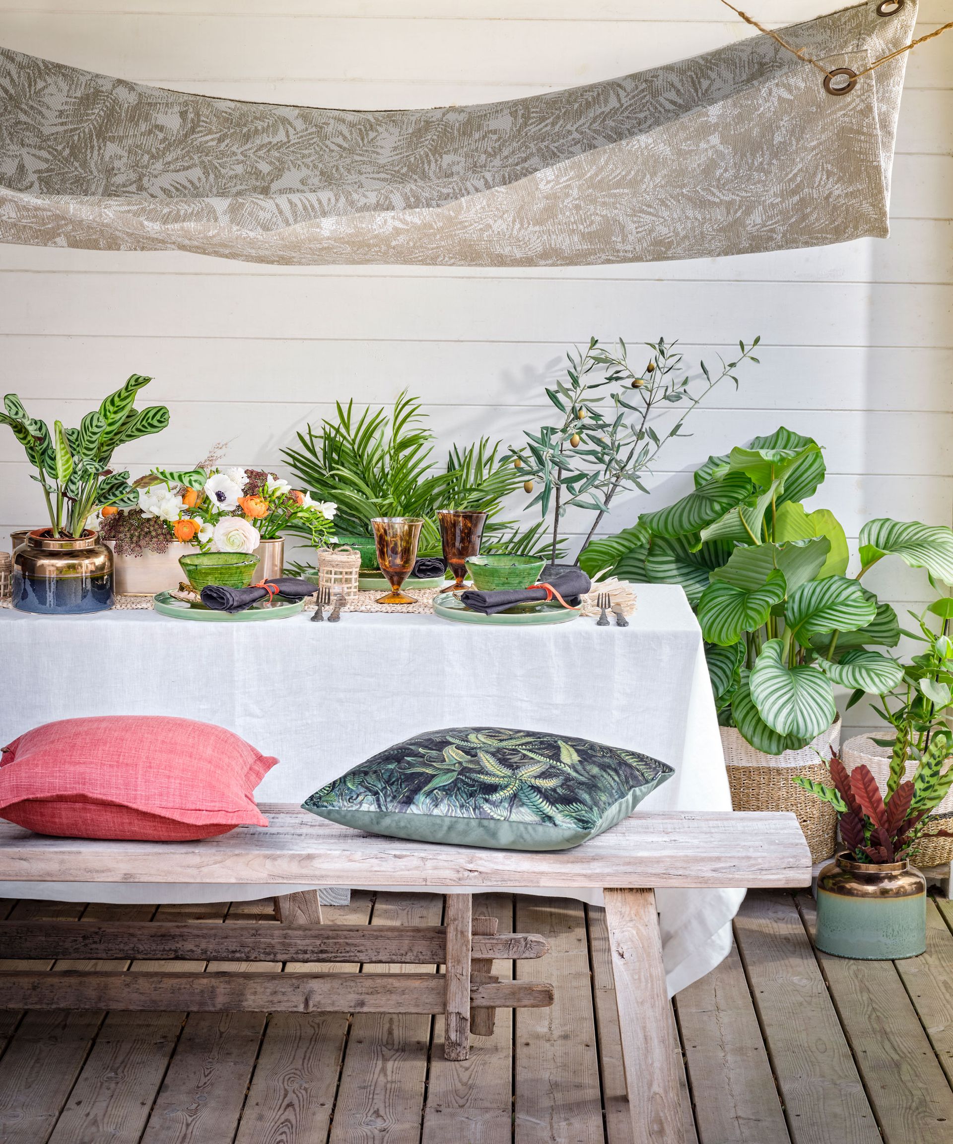 An example of outdoor dining ideas showing an al fresco dining space with green plants surrounding a table with bench seats and cushions