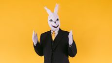 A businessman wearing a costume bunny head and white gloves.